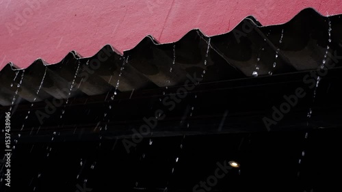 A building with a red roof and a black gutter. The gutter is filled with rainwater, and the rain is falling from the roof. Scene is somber and melancholic