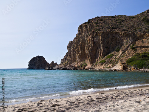 Fototapeta Naklejka Na Ścianę i Meble -  Sunlit beach with gentle waves, warm sand, and stone cliffs — a typical Greek summer landscape.