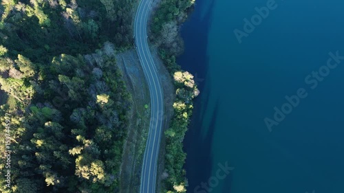Scenic winding road alongside tranquil blue lake surrounded by lush greenery in a serene natural setting