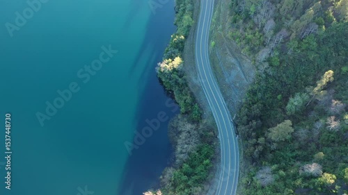 Scenic winding road alongside tranquil blue lake surrounded by lush greenery in a serene natural setting