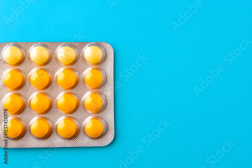 Top-down view of blister pack of yellow cough lozenges or medicine tablets against blue background, flat lay.