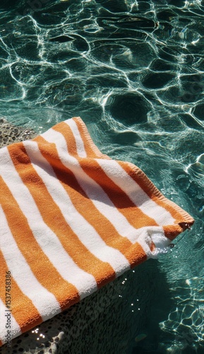 Stripes of Orange and White Towel Next to Clear Water on a Sunny Day.