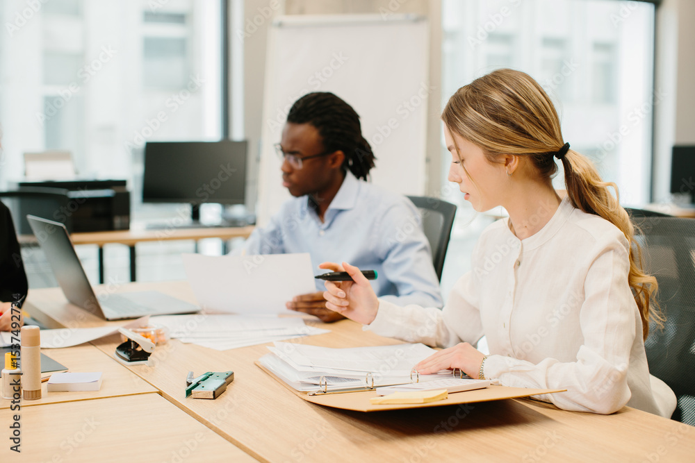 Obraz premium Focused businesswoman reviewing documents in modern office with diverse team