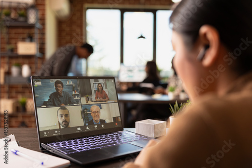 Fotografie Selective focus on laptop displaying group of coworkers on a videoconference call with a businesswoman wearing earphones