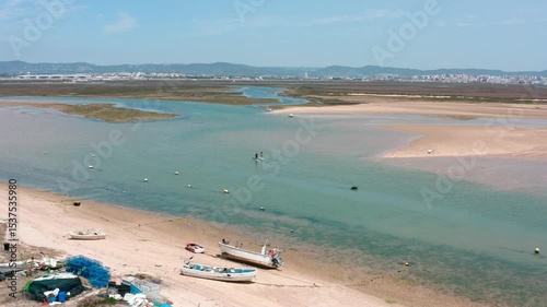 Natural park landscape in algarve region featuring shallow, calm waters with tourists paddle boarding, enjoying sunny weather and recreational water activities near ria formosa coastal environment