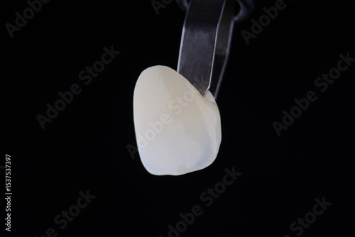 Close up shot ultra thin dental zirconium crown is held with tweezers with black background.