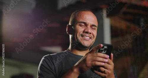 Latin Hispanic man of African descent using smartphone outdoors with slight surprise, reacting to online content while holding phone with both hands in evening setting