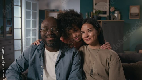 Medium portrait of happy female army officer in khaki uniform t-shirt, with identification tag sitting on couch with African American husband and biracial son, looking at camera, smiling