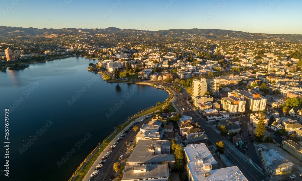 Fototapeta premium Aerial view of Lake Merritt in Oakland, California, USA, at sunrise. The photo shows the lake, the city skyline, and the surrounding hills. The light is golden and warm.