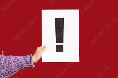 Woman holding paper sheet with exclamation mark on color background, closeup