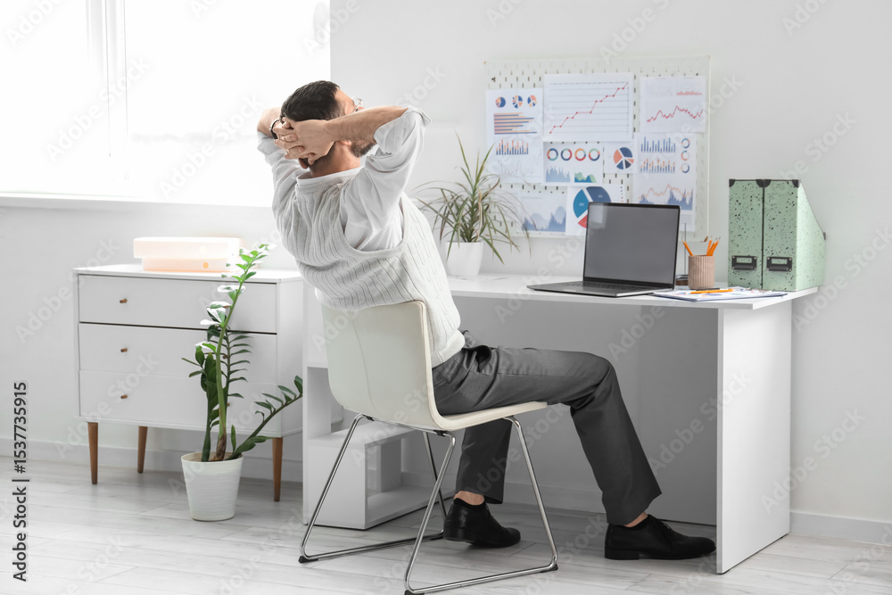 Naklejka premium Young man with blank laptop sitting at table in office, back view