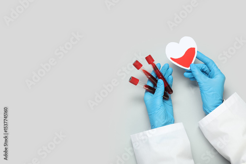 Fototapeta Naklejka Na Ścianę i Meble -  Female doctor's hands with paper heart and test tubes of blood on grey background. Blood donation concept