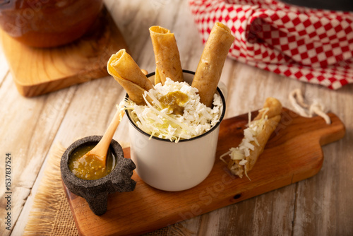 Flautas Ahogadas (Drowned Flautas) Golden tacos made with fried corn tortillas, filled with chicken or beef, and served in a glass or cup containing salsa or broth, lettuce, sour cream, and cheese.