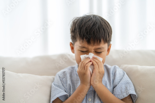 Young asian boy sneezing or blowing his nose and mouth with tissue, cold allergies or illness, health, virus and flu season, RSV, Influenza, childcare and hygiene practices, especially for children