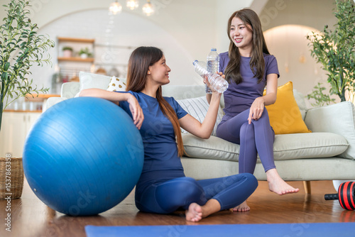 Two woman sitting relax and feeling fresh in activewear drinking water hydrating after workout at home, fitness recovery, refreshing break moment, healthy lifestyle, mineral water and wellness concept