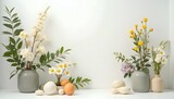 Floral still life with daisies, yellow flowers, eggs, and gourds on a white surface.