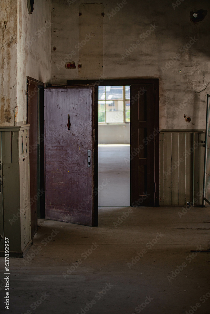 Obraz premium Abandoned industrial hall with old furniture, metal parts, and dusty workspaces. Atmospheric lost place showing decay, machinery remnants, and natural light through large windows.