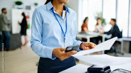 Businesswoman holding smartphone and papers near printer in modern office with diverse colleagues in suits, teamwork, corporate environment.