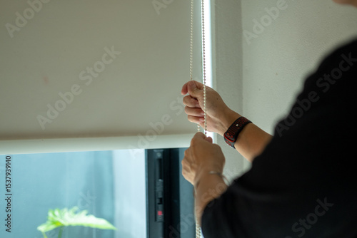 A woman's hand is pulling down the curtains to let in sunlight.