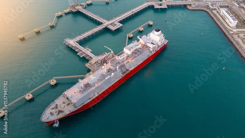 Aerial view of an LNG tanker docked at an offshore terminal with multiple pipelines, storage tanks, and an industrial complex. Captures global energy logistics