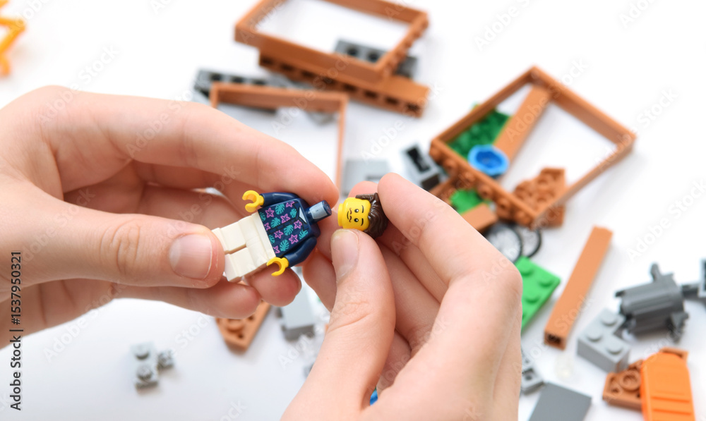 Fototapeta premium Lego bricks on the table, child is building a minifigure. Editorial illustrative image of popular plastic blocks.