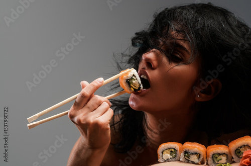 Sushi closeup in sexy woman mouth. Sexy woman eating sushi with chopsticks. Model eat sashimi. Sensual bite of sushi. Female tasting nigiri. Lunch at Japanese restaurant. Desire for delicious sushi.
