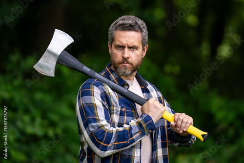 Handsome man or lumberjack in checkered shirt hold axe. Lumberjack or woodman. Masculinity concept. Man brutal strong attractive guy cutting wood with axe in forest. Lumberjack with big axe in forest.