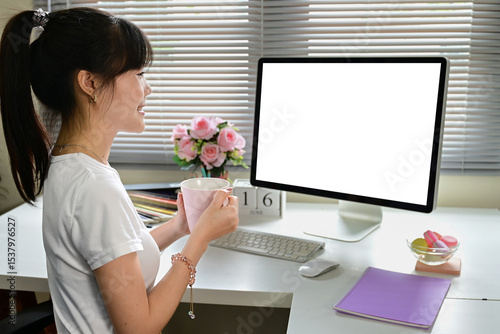 A woman is sitting at a desk with a computer monitor and a cup of coffee. She is smiling and she is enjoying her work. The desk is well-organized with a keyboard, mouse, and a bowl of candy