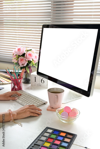 A woman is typing on a computer at a desk with a pink mug and a bowl of Macarons