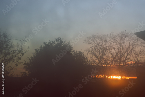 sunrise through fogged up window with droplets and silhouettes of trees and houses