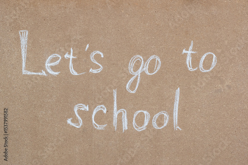 Written in chalk on a wooden slab is “Let's go to school”. The concept of the primary school year.