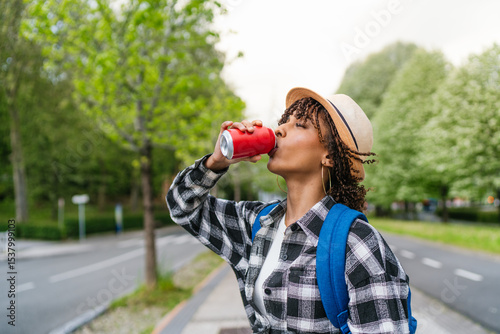 Canvastavla Young latin student drinking a refreshing soda from a can while walking on the s