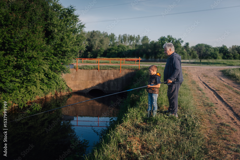 Grandfather and grandson fishing together in a canal on a sunny day Grandfather and grandson fishing together in a canal on a sunny day