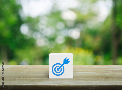 Target with dart flat icon on white block cube on wooden table over blur green tree in park, Business success concept