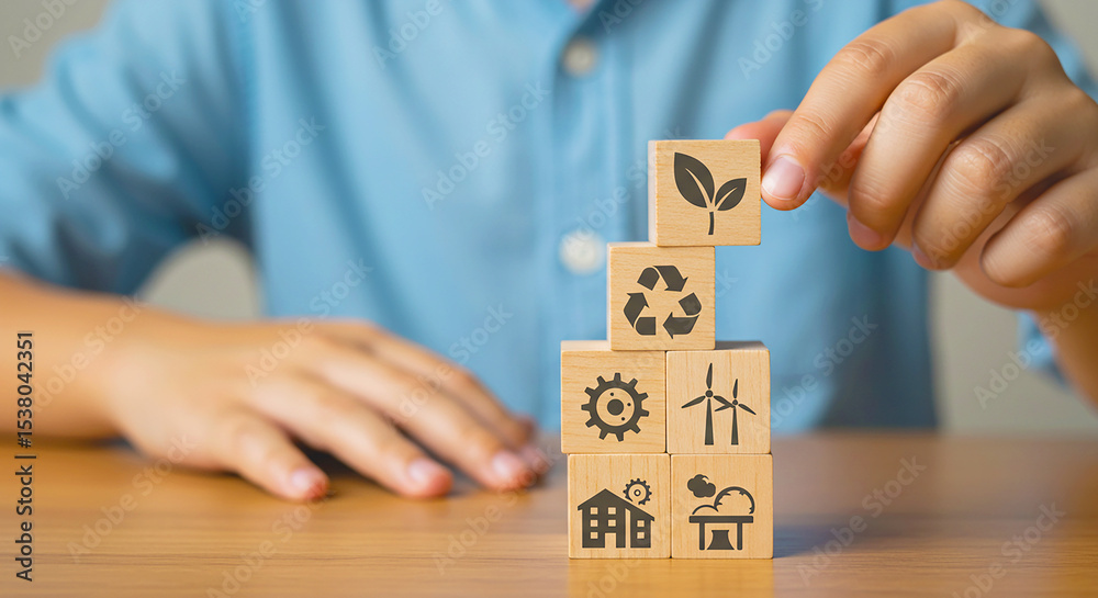 Obraz premium Person stacking wooden blocks with ecology symbols on a wooden table in a bright setting indoors