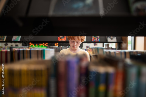 Young boy stands alone reading book in quiet library