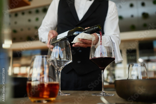 Принти на полотні Unrecognizable waiter pouring red wine into glass, wearing formal vest, standing