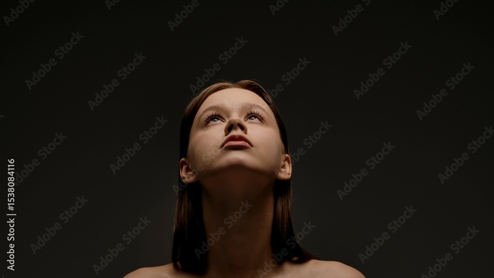 Fototapeta premium Portrait of Woman Looking Up Against Dark Background