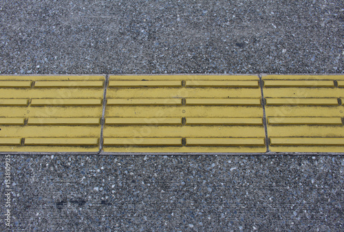 Yellow blocks of tactile paving for blind handicap. Tactile pavement for the visually impaired close up background. Texture of asphalt road with Braille blocks in the street.