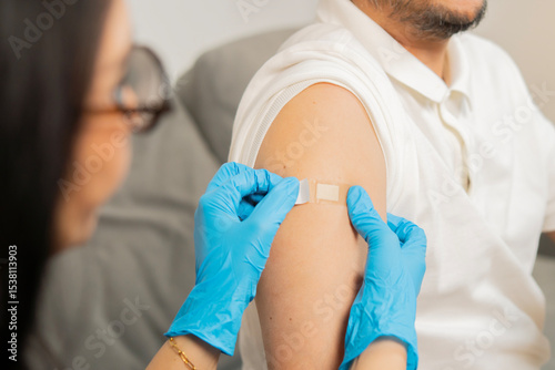 Doctor putting a bandage on the adult patient man after get a vaccinated against coronavirus at clinic.