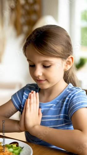 Girl with hands clasped sitting at the table before a plate of noodles and vegetables