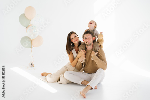 Happy family of three, father, mother and two child boy, are posing for a photo in front of a bunch of balloons