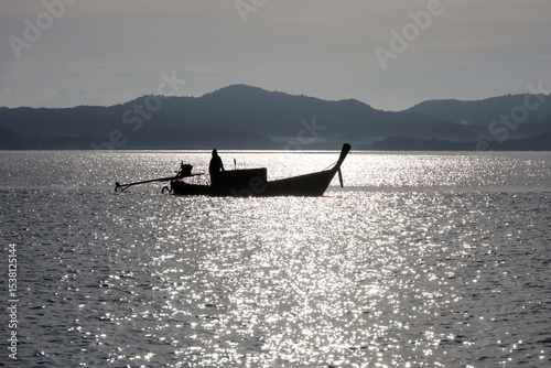 Silhouette of fisherman in fishing boat with motor in the Andaman sea on mountain coast background