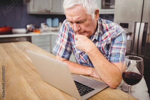 Silver laptop sitting open on wooden table in modern kitchen with glass of red wine