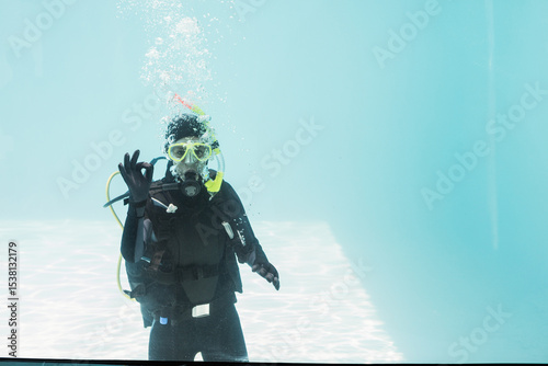 Scuba diver wearing yellow dive mask and scuba tank floating in clear pool water, bubbles rising