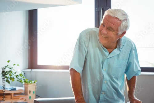 Senior man leaning on table in bright workspace with potted plant and stacked boxes, copy space