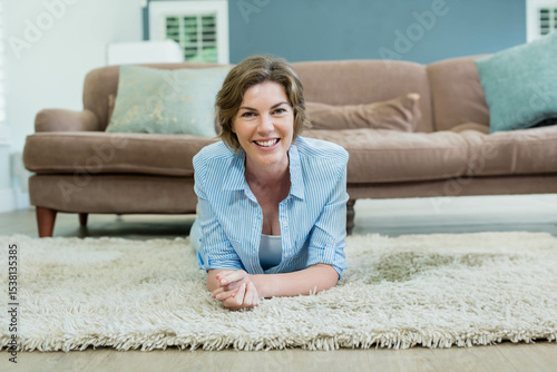 Woman in her 30s lying on plush shag rug in living room with brown sofa, smiling