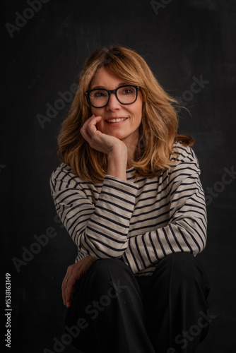 Studio portrait of a blond haired woman sitting against isolated dark background