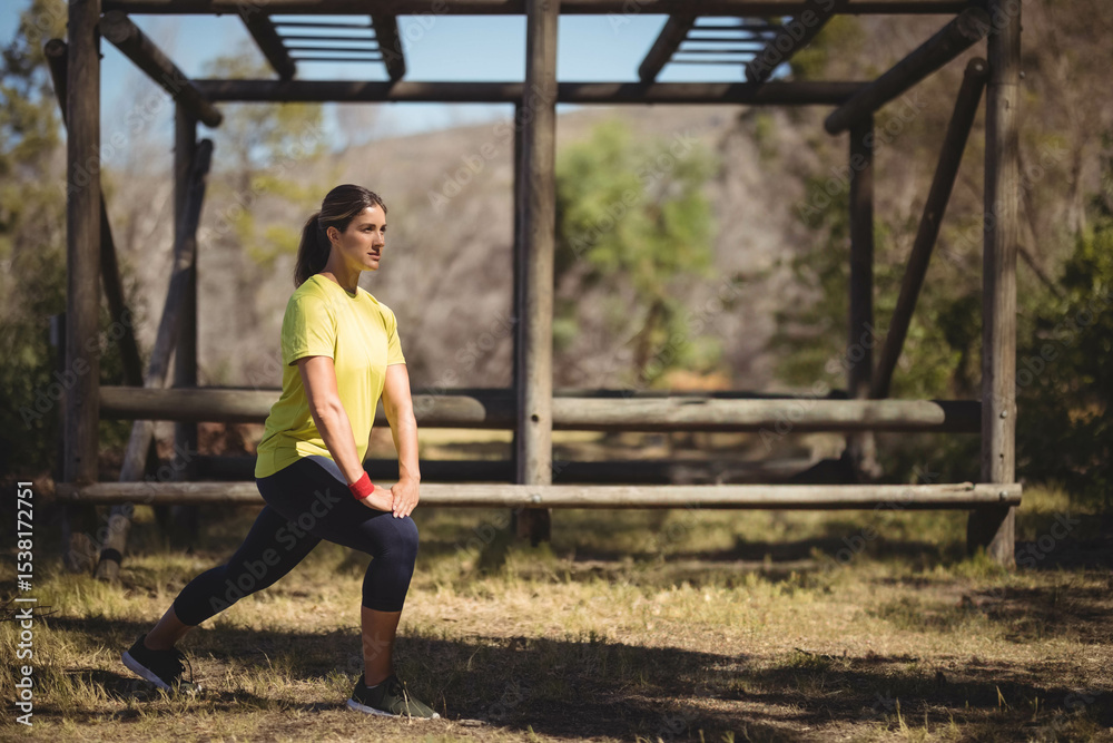 Obraz premium Woman performing forward lunge on grass by wooden obstacle beneath clear sky and wooded hills