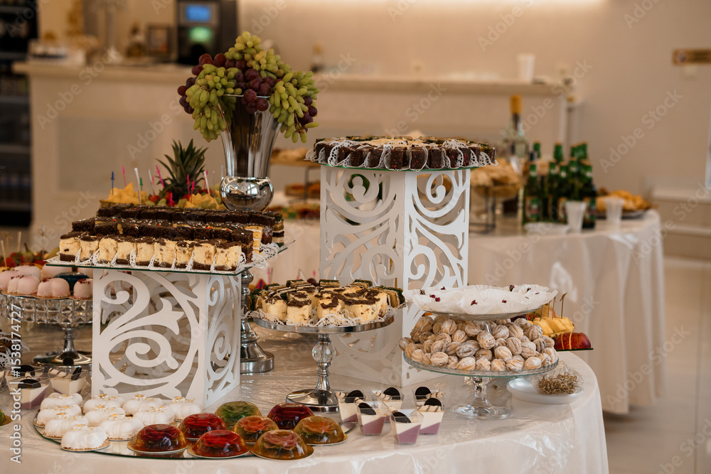 Elegant Dessert Table Setting at a Wedding Reception Featuring Chocolate Cakes, Fruit Arrangements, and White Decor Elegant Dessert Table Setting at a Wedding Reception Featuring Chocolate Cakes, Fruit Arrangements, and White Decor
